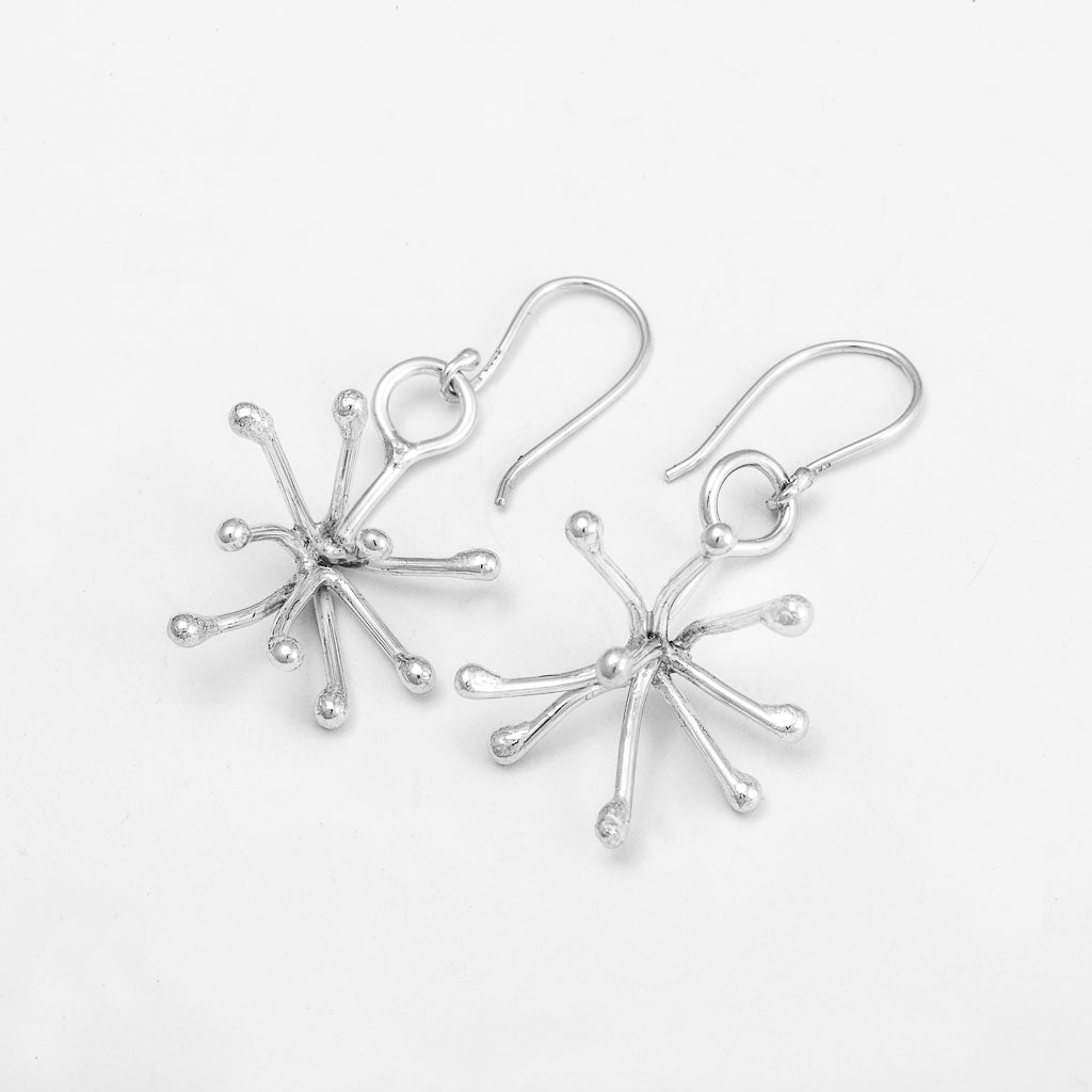 Ett par hängande novemberblommeörhängen i silver på vit bakgrund