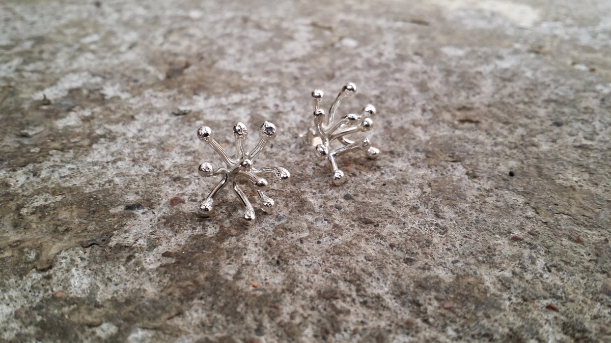 Novemberblommans handsmidda stiftörhängen i silver – ett par på stenbakgrund